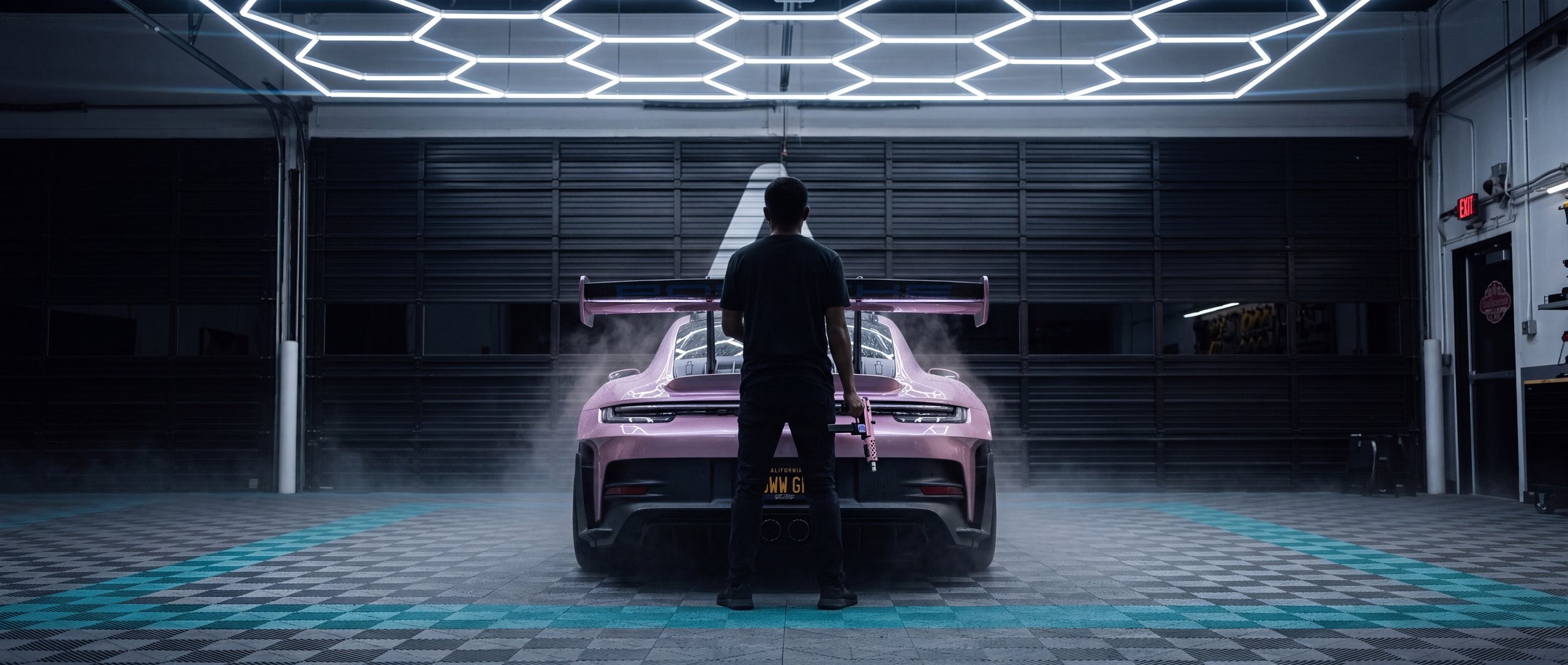 Detailer holding the pink Apex Flamingo beside a pink 911 in the Apex bay